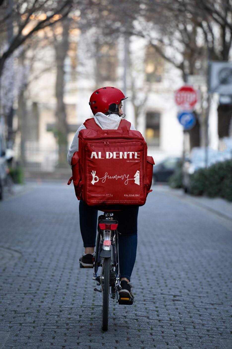 A courier cycling with a red Al Dente delivery backpack
