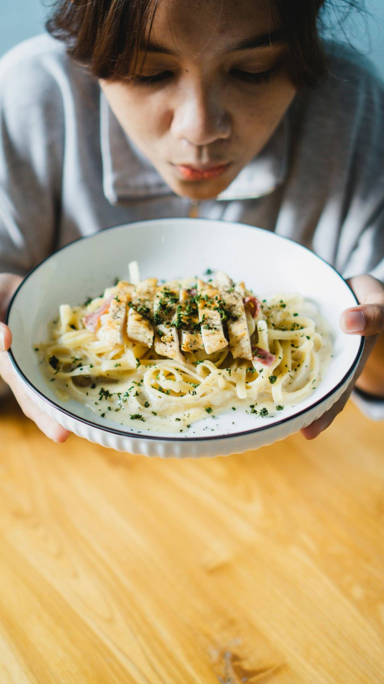 A guest leaning over a bowl of creamy chicken pasta